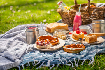 Picnic duvet and basket with different food, fruits, cake and pretzels on green grass in a park