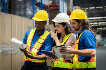 Three workers in safety gear are looking at a tablet. They are wearing reflective vests and hard...