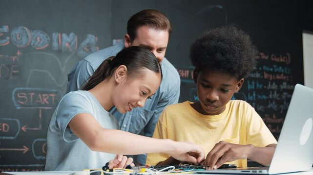 Caucasian teacher talking about electric tool while student fixing robotic model on table with electronic equipment placed. Diverse academic children learning about main board structure. Edification