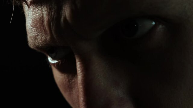 Intense close-up of a man's furrowed brow and piercing gaze, expressing anger, tension, and determination in dramatic low-light