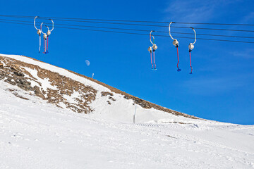 empty drag lifts on a black track against a blue sky and a white moon in an italian ski resort in...