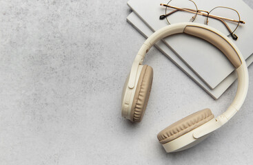 Modern wireless headphones lying on table next to books and eyeglasses
