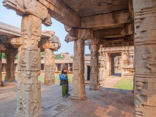 Woman exploring amazing temple complex at Hampi, world famous unesco site. Tourist walking among ruins stone walls gateways in Karnataka, India