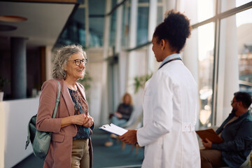 Obraz premium Happy elderly woman communicating with her doctor in hospital hallway.