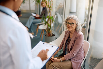 Senior woman communicating with doctor in waiting room at clinic.