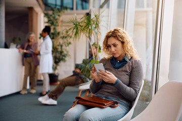 Mid adult woman using mobile phone in waiting room at doctor's office.