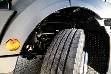 Front view of a commercial truck’s tire under the wheel arch, showing detailed tread design,...