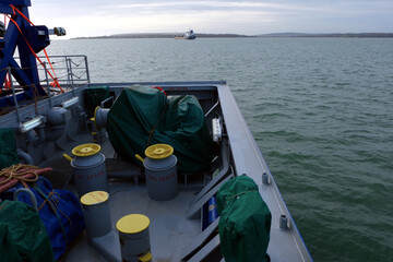 Mooring winches situated in aft stern manoeuvring station with bollards, bitts and ropes of heavy load carrier vessel. Winches and windlass are covered with green tarpaulin.