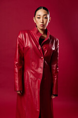 Fototapeta premium Beautiful asian woman in a red leather coat posing against a red background