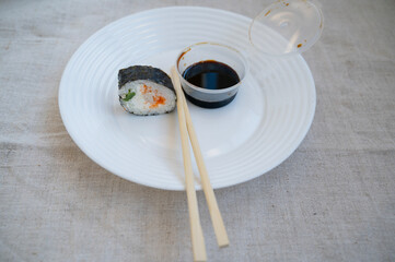 sushi roll with chopsticks and wasabi sauce in a plastic container on a white plate.
