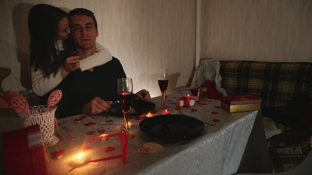 Happy loving young man making proposal for marriage to young woman sitting at table with candles, marry me. Romantic couple having dinner celebrating engagement. Valentines day concept