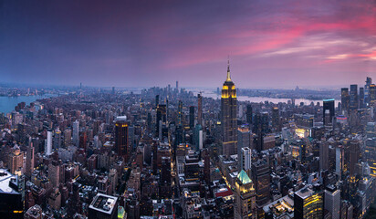 Aerial view of Manhattan at dusk with glowing city lights and dramatic sunset clouds. Bright...