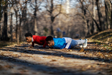 Two black strong sportsmen doing pushups in nature on fitness day.