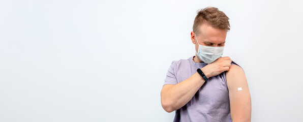 A young man lifts the sleeve of his shirt, showing the patch at the vaccination site
