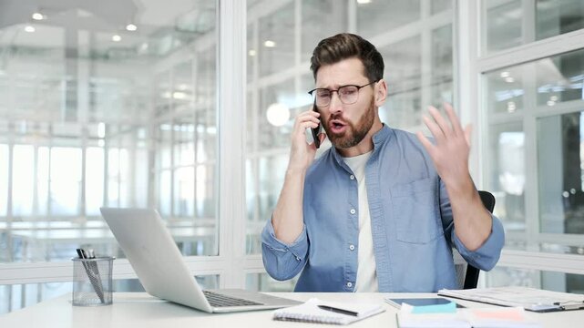 Angry businessman arguing talking on mobile phone sitting at workplace in office. Excited dissatisfied manager solving stressful business situation or conflict resolution. Boss scolds the subordinate