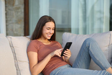 Happy woman in a terrace at home using mobile phone