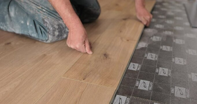 Renovation, construction, flooring and people concept - close-up of a man installing a wooden floor.