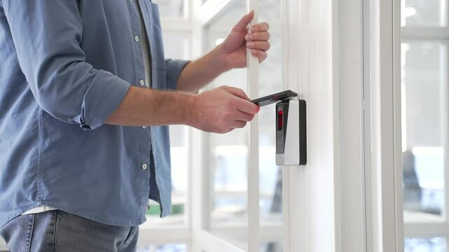 Close up of businessman unlocking door using mobile phone application. Unlocks a modern glass white office. Scanning open smartphone with mock up screen app. Smart electronic locks with keyless access