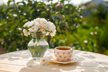 Summer still life. Beautiful roses flowers stand in a vase on a wooden table with a cup of tea.
Relaxation in the village on a sunny day. The joy of summer.