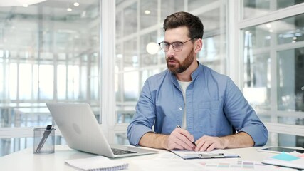 Busy businessman doing paperwork using laptop sitting at desk at workplace in business office. Confident financier working fills out documents, writing, making a tax return or engaged in accounting