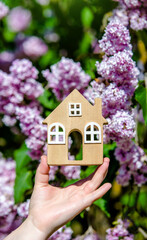 The girl holds in her hand the symbol of the house against the background of blooming lilac
