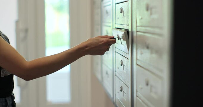 Woman is opening her mailbox inside a cluster of mailboxes for her apartment. Mail shipping concept.