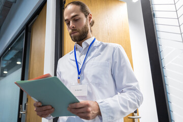 Fototapeta premium Male doctor standing in hospital corridor holding case history and medical documents