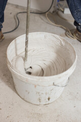 Making white thick putty in a bucket with an electric mixer - building material for interior wall finishing