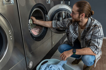 Positive man in self service commercial laundry using washing and drying machine