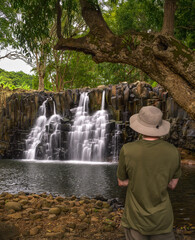 A tourist in a green shirt and hat observes the scenic Rochester Falls in Mauritius.