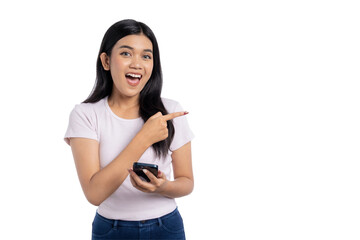 Young Asian woman pointing at copy space and holding mobile phone, looking excited and happy, isolated on transparent background
