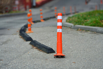 Damaged safety delineator with torn out fastening. Broken road infrastructure, plastic traffic cone. Orange traffic cones with reflective stripes guide vehicles along paved road. Selective focus