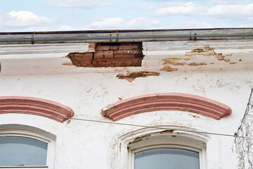 Decaying historic building with visible wall damage, chipped paint, crumbling roof edges,...
