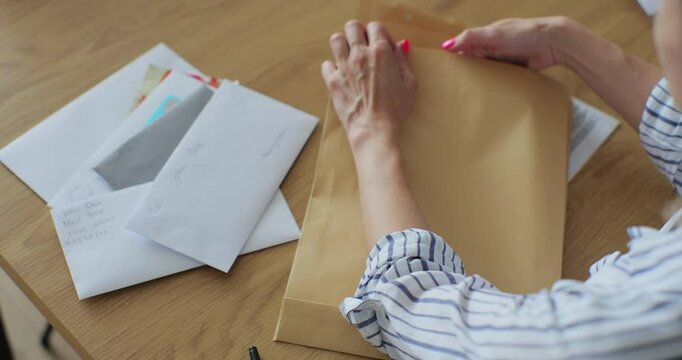Close up female hands putting letter in envelop return form. Woman sends a return form by letter.
