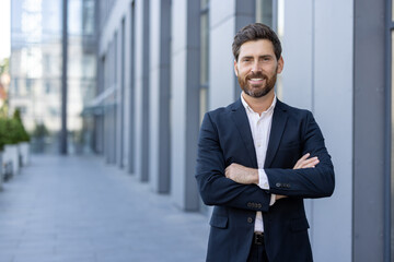 Portrait of successful businessman outside office building. Mature man in business suit smiling and...