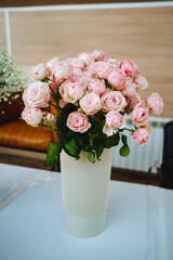 A beautifully arranged dining table showcases a ceramic vase brimming with fresh pink roses, significantly enhancing the charm of the room and captivating the attention of everyone present