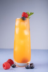 refreshing tall glass of orange juice cocktail garnished with fresh raspberries, blueberries, and mint on a soft blue background capturing a vibrant and inviting summer mood, thirstquenching