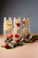 three refreshing glass tumblers filled with sparkling water, vibrant lime, lemon, raspberries, and blueberries, set against a cool, neutral background with scattered fresh leaves. natural, diet