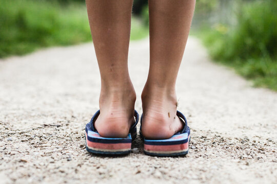 Rear view close-up of a boy's dirty feet wearing flip flops