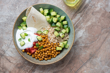 Plate with roasted chickpeas, vegetables, yogurt and rice, horizontal shot on a brown granite background with space, flat lay