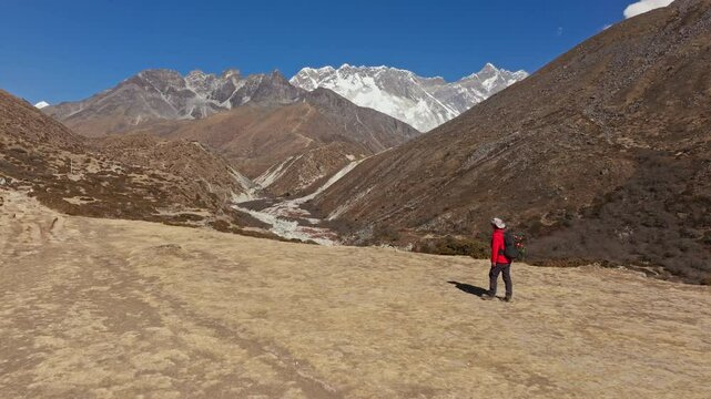 Aerial close up of lone hiker walking steep alpine path amid towering Himalayan peaks, in Shomare to Dingboche Route among snow covered summits