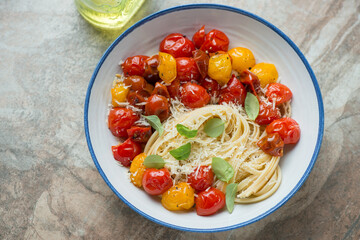 White and blue plate with roasted cherry tomatoes and linguine, horizontal shot on a brown granite background, elevated view