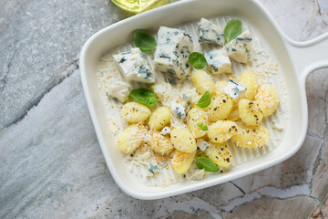 Beige serving tray with potato gnocchi, blue cheese and basil, horizontal shot on a grey granite background, high angle view