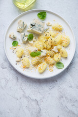 Plate of italian potato gnocchi served with blue cheese, vertical shot on a white stone background with space, elevated view