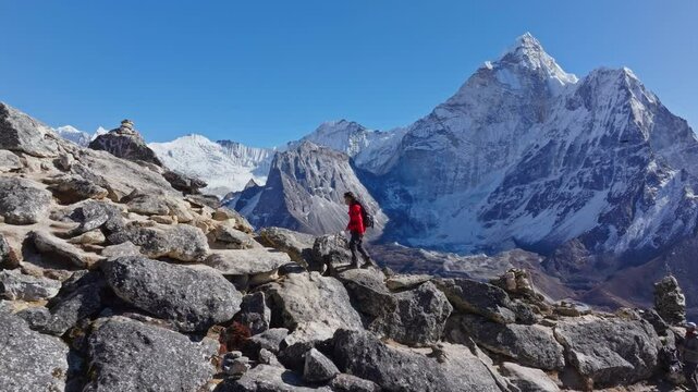 Mountaineer navigates rocky ridge, wearing red jacket, prayer flags fluttering, Mount Everest peaks rising behind gus body