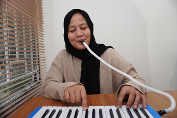 Asian muslim woman playing pianica, melodica blow organ musical intrument