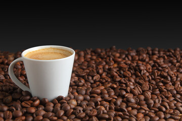 White Cup of Espresso coffee Surrounded by Dark Roast Coffee Beans