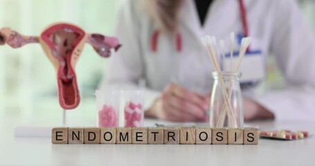 Female doctor focuses on papers at desk with blocks showing Endometriosis near model of uterus. Concentration on endometriosis awareness and treatment