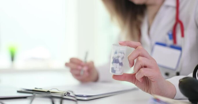 Lady doctor holds small bottle of pills in hand while writing on clipboard. Medical consultation prescription and documentation in healthcare setting