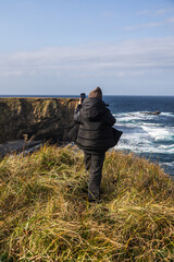 A woman admires the natural landscape on the island of Iturup and wants to take a photo on her phone. Vertical photo